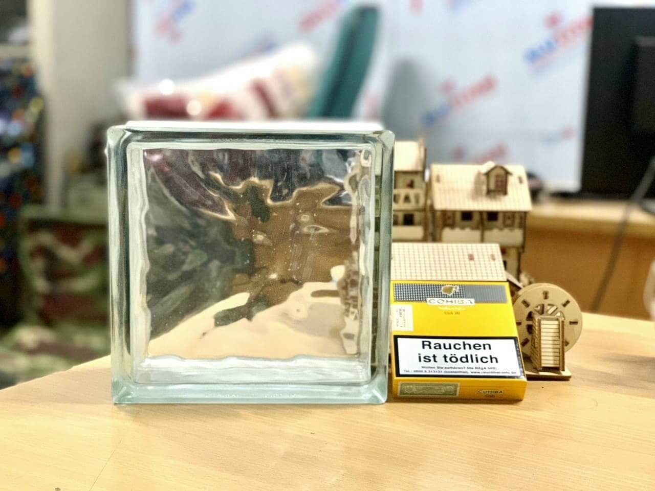 Khối thủy tinh bên cạnh hộp thuốc lá có cảnh báo tiếng Đức trên bàn gỗ.