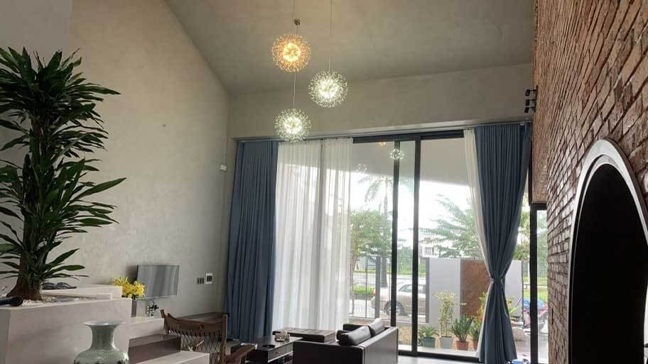 Phòng khách hiện đại với đèn treo lấp lánh và cửa kính lớn nhìn ra vườn, mang không gian thoáng đãng.