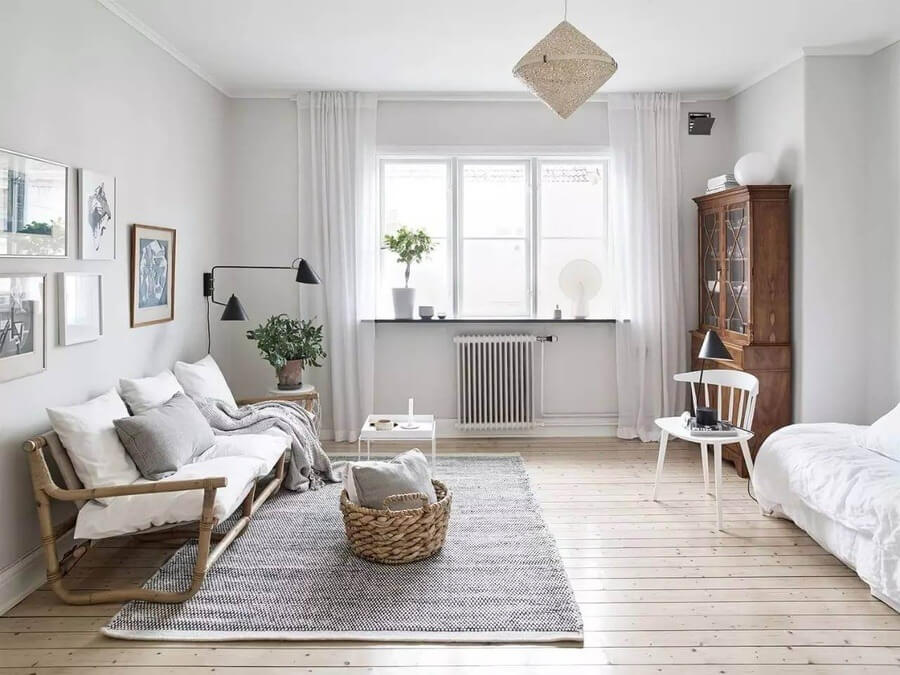 Phòng khách tối giản với sofa gỗ, bàn trắng, cửa sổ sáng và tường trắng, cây xanh tạo điểm nhấn, phong cách Bắc Âu.