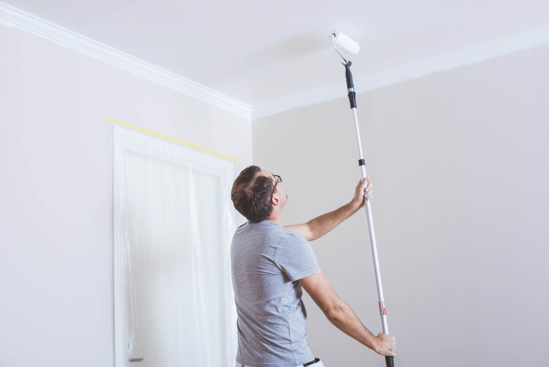 Người đàn ông sơn trần nhà bằng con lăn sơn, làm mới không gian sống gia đình.