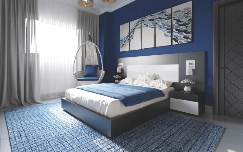 Phòng ngủ hiện đại với tông màu xanh, giường đôi và ghế treo cạnh cửa sổ lớn.