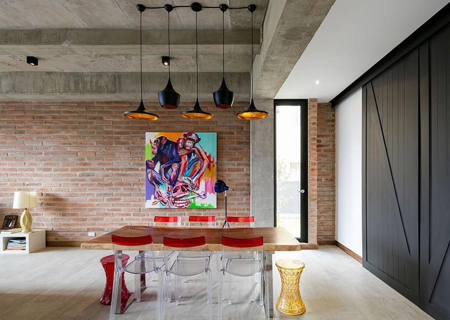 Phòng ăn hiện đại với tường gạch, bàn ghế trong suốt, đèn treo và tranh nghệ thuật sống động.