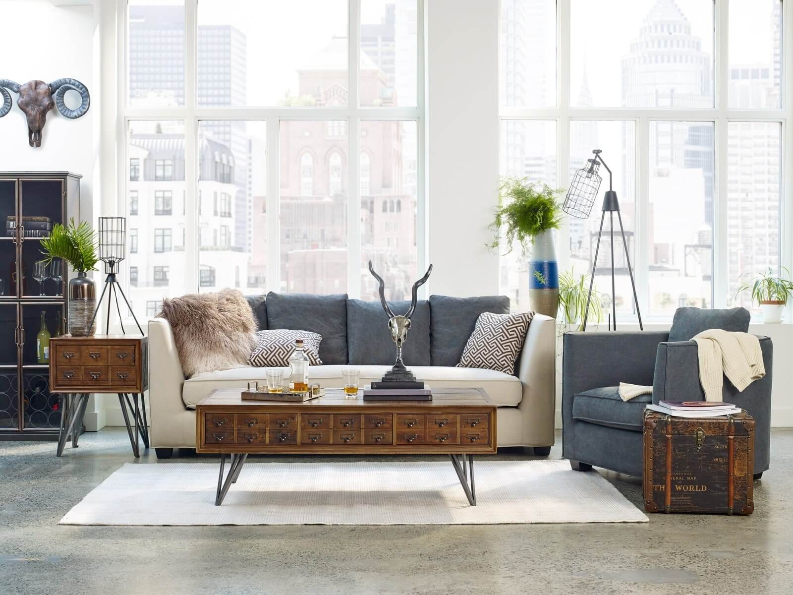 Phòng khách hiện đại với sofa, ghế bành xanh, bàn cà phê gỗ, cây xanh và cửa sổ lớn nhìn ra thành phố.