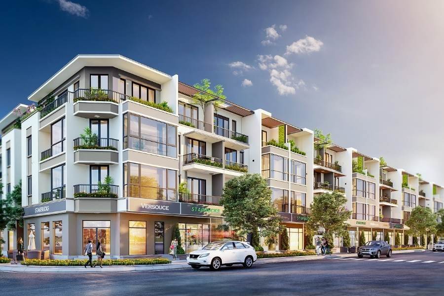 Dãy nhà phố hiện đại với cửa hàng tầng trệt, xe cộ lưu thông và trời xanh nắng nhẹ.