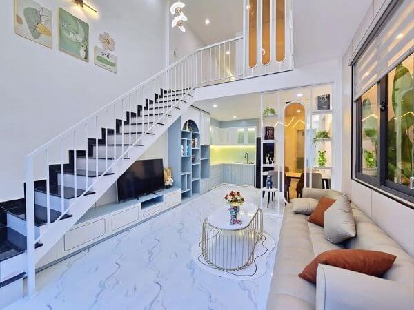 Phòng khách hiện đại với cầu thang trắng, sofa, bàn trà và kệ TV, thiết kế nội thất tối giản và sáng sủa.