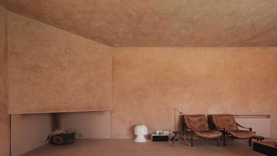 Phòng khách tối giản với ghế da, tường và trần màu nâu, bàn nhỏ và đèn bàn trắng.