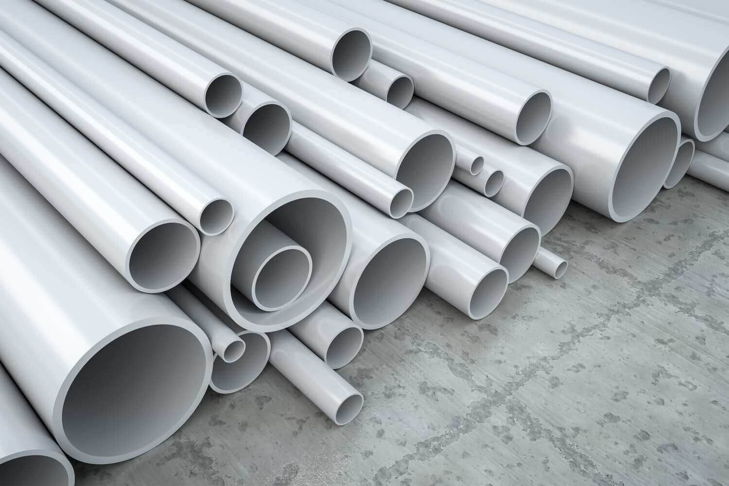Ống nhựa PVC màu trắng xếp chồng lên nhau trên nền bê tông, nhiều kích thước khác nhau.