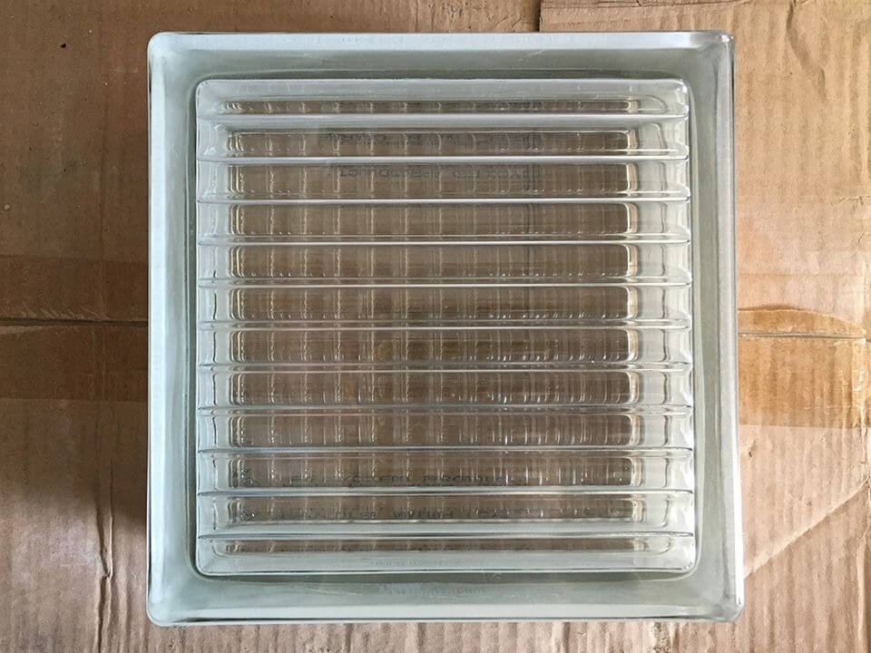 Khối kính thủy tinh hình vuông với bề mặt sọc ngang, đặt trên bìa carton, dùng trong thiết kế nội thất và xây dựng.